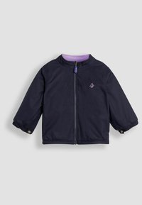 Tamsiai mėlyna striukė su užtrauktuku, stovinčiu coleru ir elastingomis rankovėmis. Viduje turi violetinę pamušalą ir logotipo detalę ant krūtinės.
