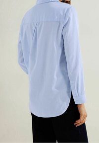 Ljust blå rutig skjorta med knappar och långa ärmar, ryggparti, rundad nederkant och manschettdetaljer. Tillverkad av ett mjukt tyg med subtil textur.