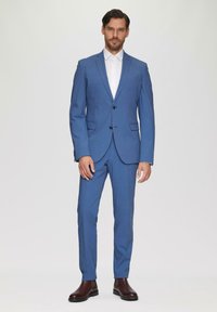 Helles blaues Anzug mit taillierter Passform, ausgestattet mit zwei Knöpfen, Reverskragen und einer Brusttasche, kombiniert mit einem weißen Hemd und braunen Schuhen.