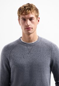 Grijze gebreide sweatshirt met een ronde hals en raglanmouwen, met een zachte textuur en een subtiel gemêleerd patroon. Geen zichtbare logo's.