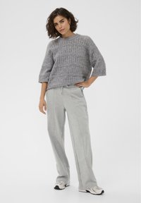 Hall hallitatud kampsun soonikkoes mustriga ja laiade varrukatega, mida on kombineeritud helehallide dressipükste ja spordijalanõudega. Üldine tekstuur on sile.