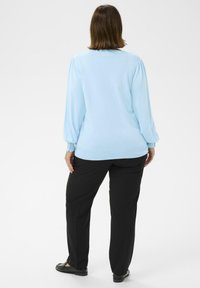 Hellblauer Pullover mit Puffärmeln, rundem Ausschnitt und gerippten Bündchen. Kombiniert mit schwarzen, gerade geschnittenen Hosen und schwarzen Schuhen.
