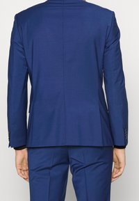 Marineblauwe op maat gemaakte blazer met gesneden revers, enkele split en knoopmanchetten. Gladde textuur, gestructureerde pasvorm en strakke lijnen.