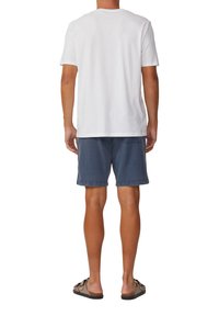 Weißes Baumwoll-T-Shirt kombiniert mit blauen Denim-Shorts. Die Shorts haben eine lockere Passform, umgeschlagenen Saum und Taschen. Sandalen vervollständigen das Outfit.
