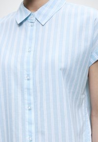 Lichtblauw overhemd met korte mouwen, witte verticale strepen en knopen aan de voorkant, met een puntige kraag.