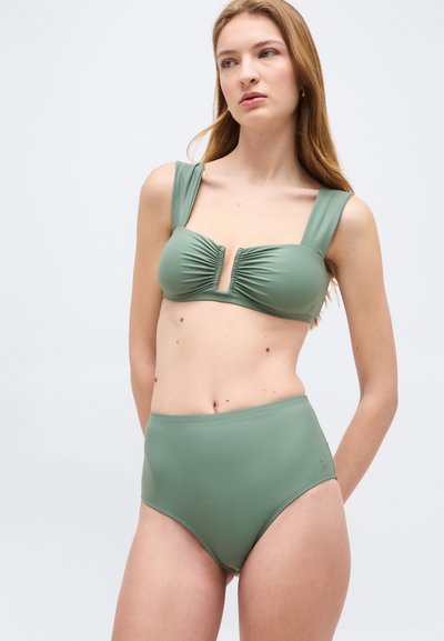 Kvinne med langt hår som har på seg en to-delt badedrakt i salviegrønn med høytlivsunderdel og en rynket overdel med brede stropper.