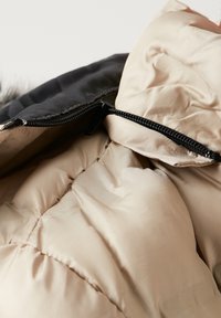 Beige puffer jacket interior with quilted texture, featuring a black zipper and a hood. The material is smooth with a slight sheen.