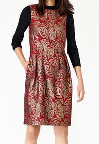 Robe rouge avec un motif de feuilles dorées et noires, corsage ajusté, jupe évasée et manches longues noires. Comprend des poches. Tissu texturé.