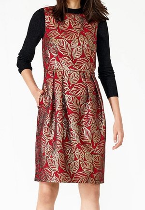 Robe rouge avec un motif de feuilles dorées et noires, corsage ajusté, jupe évasée et manches longues noires. Comprend des poches. Tissu texturé.