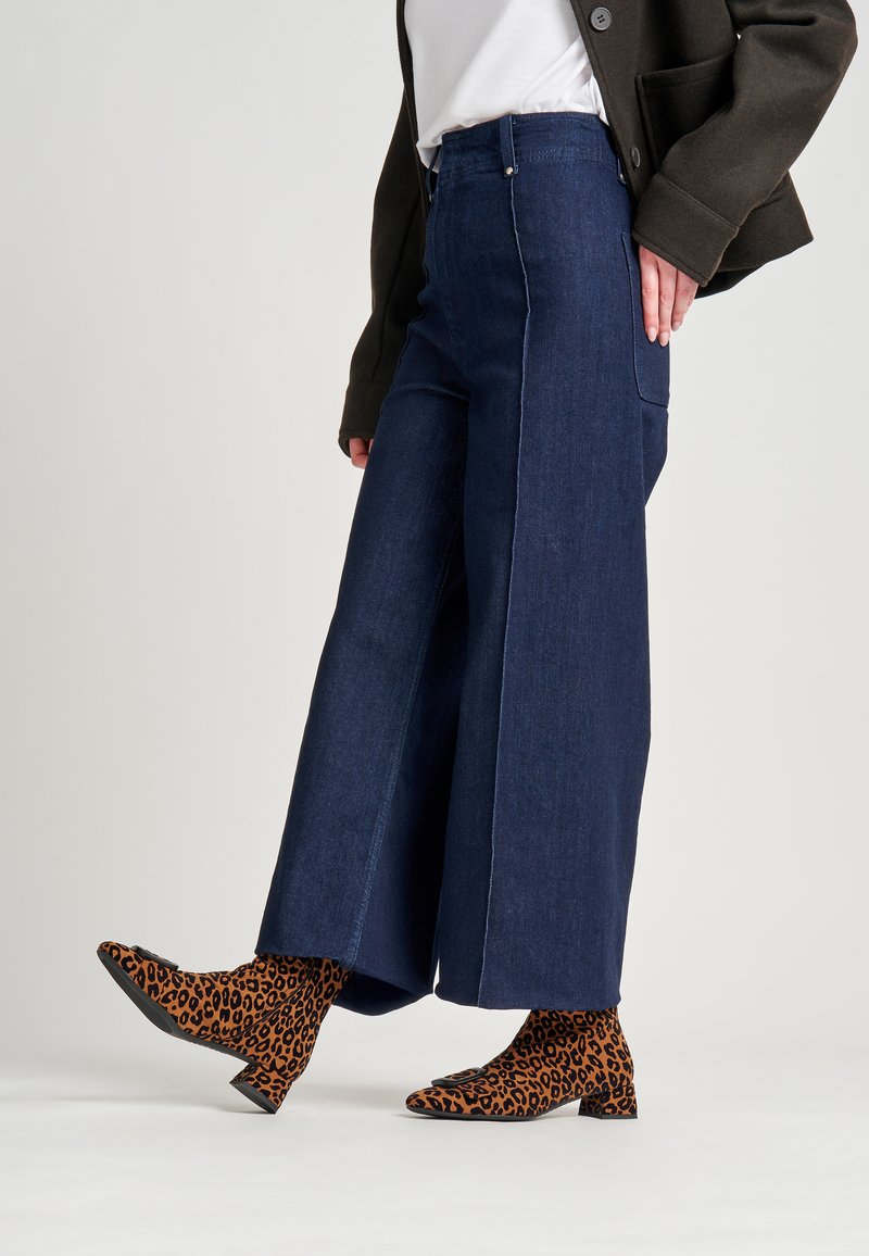 Jeans de pierna ancha azul oscuro con costuras blancas, combinados con botas de tobillo con estampado de leopardo naranja y negro que presentan un tacón bajo.