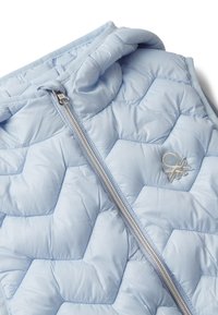 Svetle modrá prošívaná vesta s plným stříbrným zipem a vyšitým logem na hrudi, vystavená na bílém pozadí.