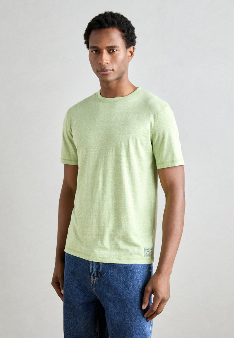 Tricou scurt cu mânecă scurtă de culoare verde deschis, dintr-un material moale și texturat, cu decolteu rotund. Asortat cu blugi din denim albastru.
