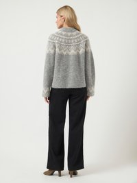 Grijze wollen trui met een ronde yoke in een wit patroon, voorzien van lange mouwen en een iets cropped pasvorm, gecombineerd met wijde zwarte broek.