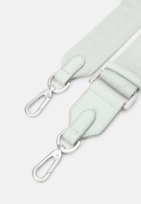 Cinturino in tessuto verde chiaro con dettagli in pelle liscia. Include moschettoni in metallo argentato lucido e dettagli di cucitura per una maggiore durata.