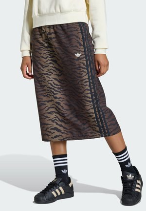 Falda midi marrón con un estampado de rayas de tigre, que incluye franjas negras a los lados y un logo bordado. Combinada con zapatillas negras y calcetines a rayas.