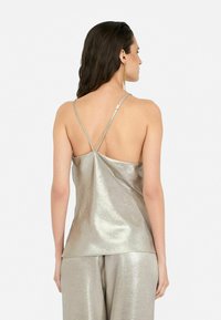 Camisola argento metallico con una vestibilità rilassata, dotata di sottili spalline regolabili e una superficie liscia. La parte posteriore presenta un design a V.