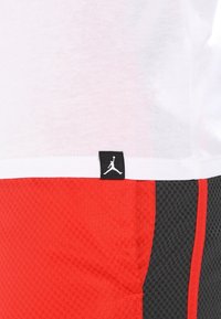 Röda och svarta träningsshorts med ett texturerat mönster, utrustade med en vit midjeband och en liten svart Jordan-logotag.