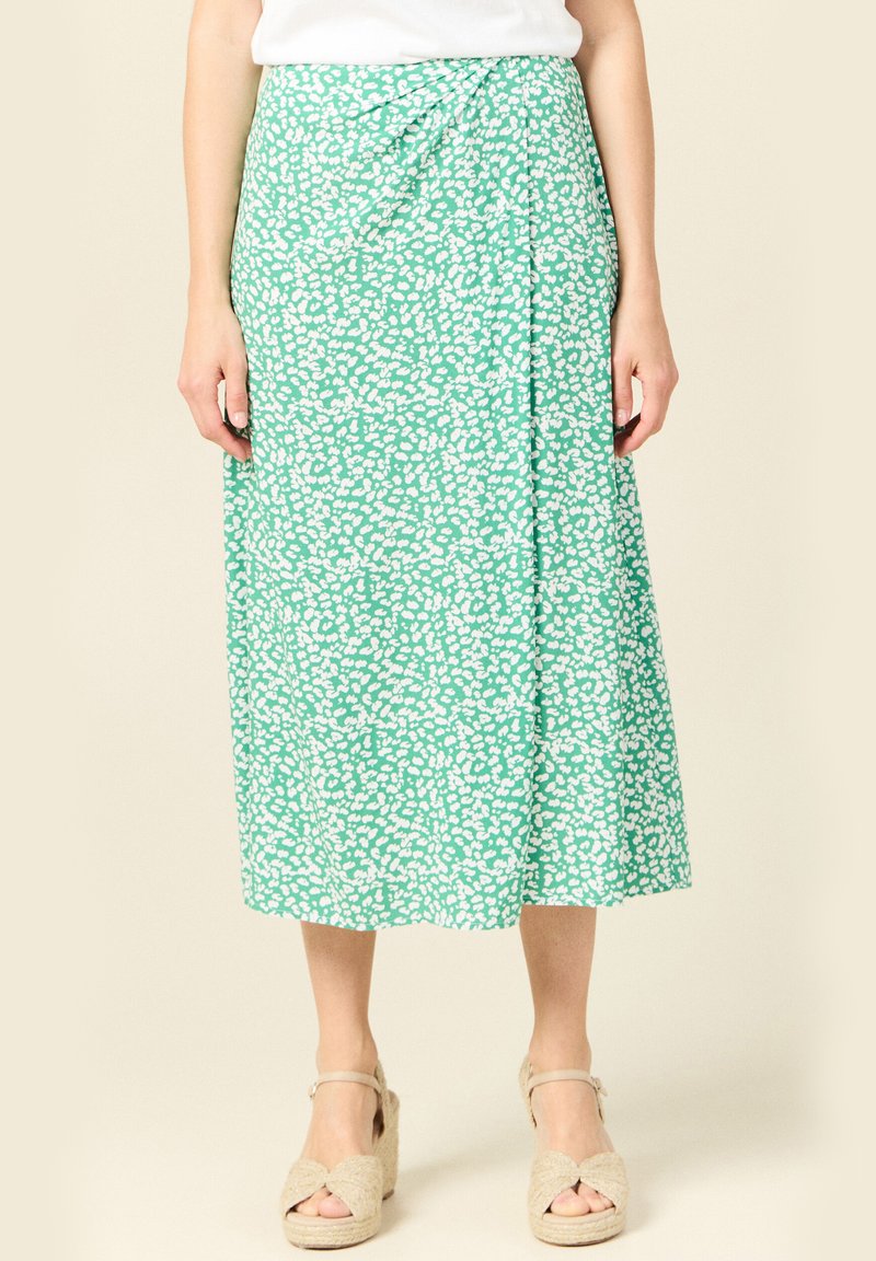 Groene midi-rok met wit abstract patroon, lichte stof, wikkeldesign, zijknopen, gecombineerd met beige wedge sandalen.