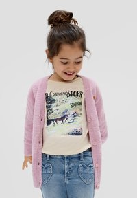 Różowy puszysty kardigan założony na beżowy t-shirt z graficznym motywem konia, w połączeniu z niebieskimi dżinsami posiadającymi kieszenie na plecach w kształcie serca.