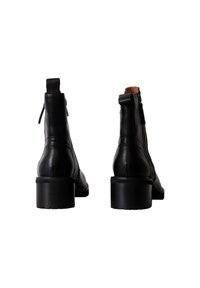 Botas de tobillo de cuero negro con un acabado suave, punta redondeada y tacón cuadrado. Presenta una cremallera lateral y una pestaña en la parte posterior.