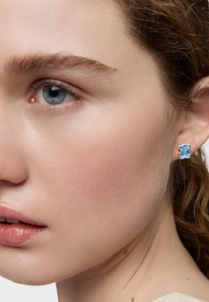 Aquamarinfarbene Bären-Ohrringe mit Silberfassung. Nahaufnahme des Ohrrings am Ohr eines Modells, die seine Farbe und Designdetails zeigt.