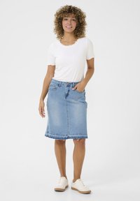 Fustă din denim albastru deschis cu margine desfăcută, buzunare frontale și talie ajustată. Asortată cu un top alb cu margini ondulate și adidași albi.