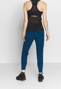 Svart atletisk tanktop med utskuret rygg, kombinerad med åtsittande turkosa byxor. Texturerat tyg och slank design, avslutad med svarta sneakers.