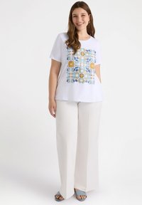 Camiseta blanca de manga corta con un colorido patrón floral y geométrico en el frente. Combinada con pantalones anchos blancos sencillos.