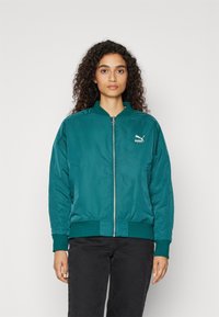 Teal satin bomberjakke med lynlåsfortil, ribbede manschetter og kant. Har et lille hvidt Puma-logo på venstre bryst.