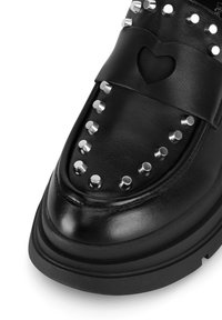 Czarne skórzane mokasyny z srebrnymi ćwiekami po bokach, wycięciem w kształcie serca i grubą podeszwą. Gładka tekstura z błyszczącym wykończeniem.