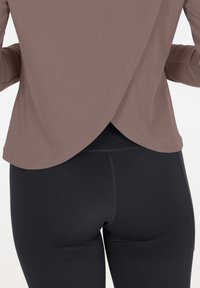 Top marrone a costine con un design incrociato sul retro, abbinato a leggings neri aderenti. Il tessuto sembra morbido con una superficie liscia.