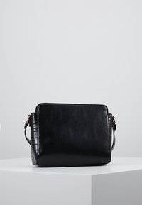 Schwarze Lederhandtasche mit glatter Textur, rechteckiger Form und einem subtilen Krokodilmuster auf einer Seite. Mit goldfarbenen Hardware-Details.