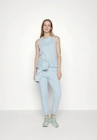 Conjunto desportivo azul claro composto por um top sem mangas e calças afuniladas, feito de tecido macio, com um detalhe em nó na cintura.