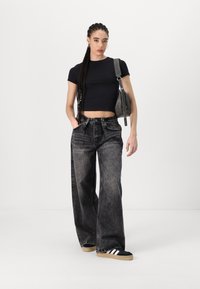 Černé zkrácené tričko, vybledlé šedé široké džíny, černé tenisky s bílými pruhy, šedá taška se strapcem, umístěné na neutrálním pozadí.