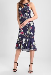 Abito floreale navy con corpino aderente, scollatura a chiave e orlo svasato. Presenta pois bianchi e vivaci motivi floreali. Tacchi neri.