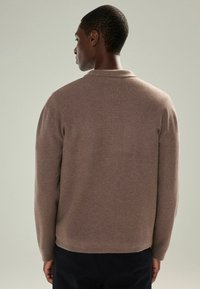 Brun strikket sweater med en blød tekstur, der har krave og lange ærmer. Skåret slutter ved taljen med en lige kant.