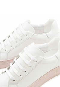 Weiße Leder-Sneaker mit runden Zehen, flachen weißen Schnürsenkeln und einer hellpinkfarbenen Gummisohle mit minimalen Nähdetails.
