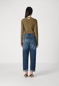 Olijfgroene lange mouw top met uitsnijding op de rug, gecombineerd met blauwe hoge taille spijkerbroeken met opgerolde mouwen en achterzakken. Bruine hakken.