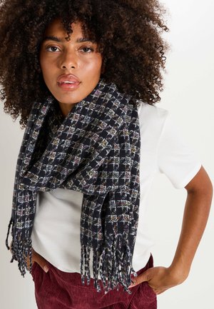 Bufanda tejida negra y multicolor con un patrón de cuadros, con extremos con flecos y una textura suave, llevada alrededor del cuello.