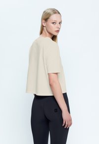 Top corto de manga corta beige, hecho de una tela suave, combinado con leggings negros de tiro alto. Diseño minimalista sin patrones o acentos visibles.