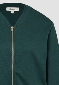 Dunkelgrün bomberjacke mit rundem Ausschnitt, vollem goldenen Reißverschluss auf der Vorderseite und glatter Textur. Verfügt über lange Ärmel und keine Muster.