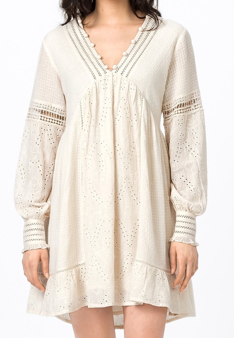Robe crème à manches longues avec broderie ajourée, insertions en dentelle sur les manches, encolure en V boutonnée et ourlet à volants juste au-dessus des genoux.