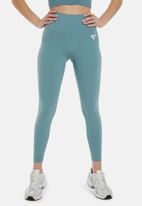 Leggings de tiro alto en azul cielo con una textura suave y elástica y un pequeño logo blanco en la cadera izquierda. Combinados con zapatillas blancas.