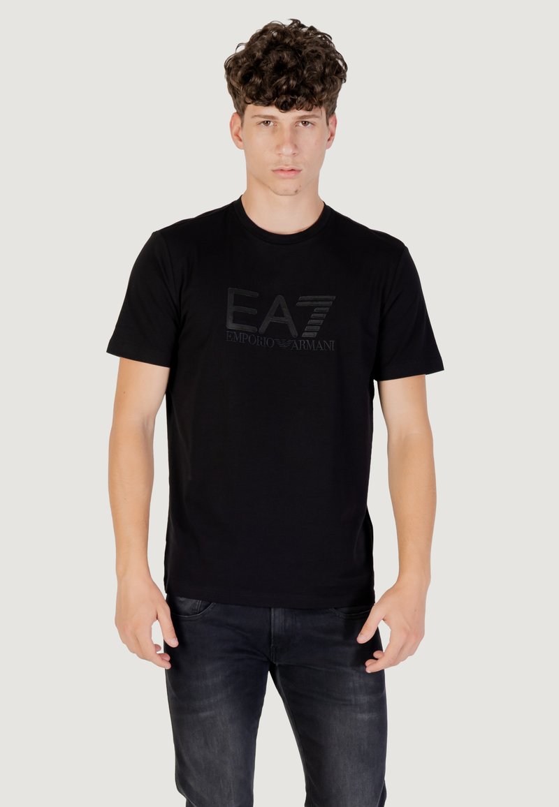 T-shirt in cotone nero con logo EA7 Emporio Armani testurizzato sul davanti, colletto rotondo e maniche corte. Pantaloni non visibili.