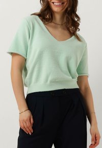Mint green, short-sleeved sweater with a v-neck and soft texture, paired with dark, high-waisted trousers featuring two buttons.