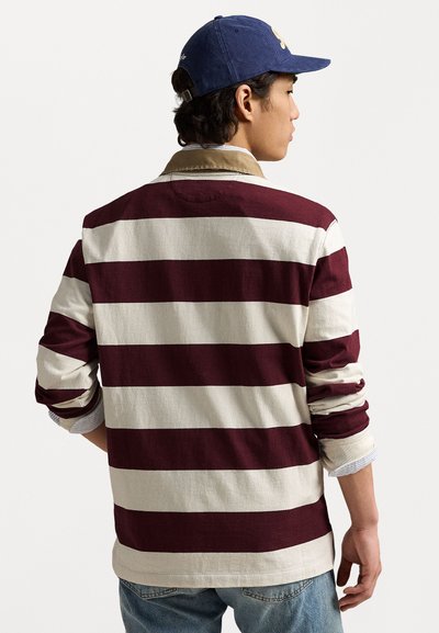 Langermet stripete skjorte med burgunder og kremfarger, knappeskjorte og oppbrettede ermer. Brukt sammen med blå jeans og en marineblå caps.