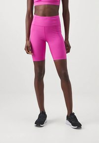 Rózsaszín sportnadrág magas derékrésszel, rugalmas anyagból készült. Fekete tornacipővel párosítva. A dizájn testhezálló sziluettet mutat.