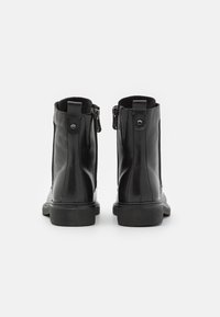 Botas negras hasta el tobillo de cuero suave, con cremallera lateral y punta redonda, suela de goma baja y detalle de costura mínima.