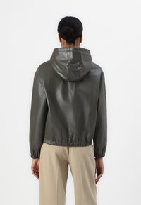 Giacca con cappuccio in finta pelle verde scuro, con vita arricciata e maniche lunghe, dal texture liscia e lucida e con polsini elastici.