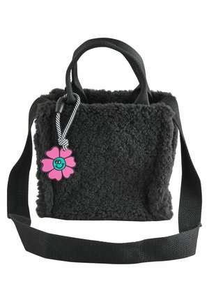 Sac à main noir duveteux avec deux poignées, une longue bandoulière et un porte-clés fleur rose souriante attaché près du haut par un cordon rayé.